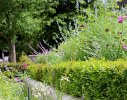 A clipped hedge and flower beds read off the architectural retaining wall